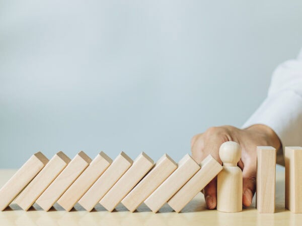 A man holding wood person model stopping wood pieces of a domino effect. Concept of risk management, risk protection, crisis and investment protection